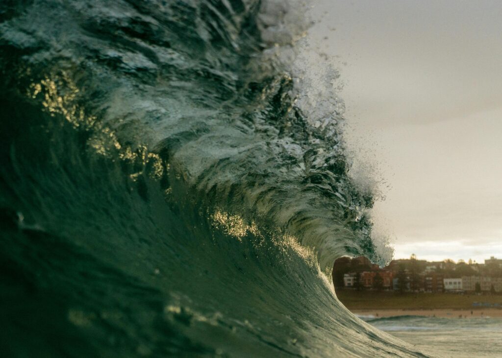 Powerful ocean wave crashing at Bondi Beach under a cloudy sky.
